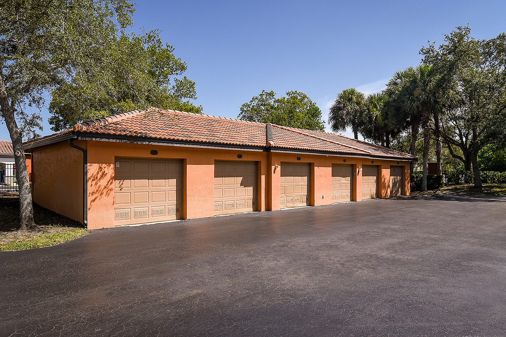 Elegant townhouse garages with terracotta roofs and lush greenery on a sunny day.