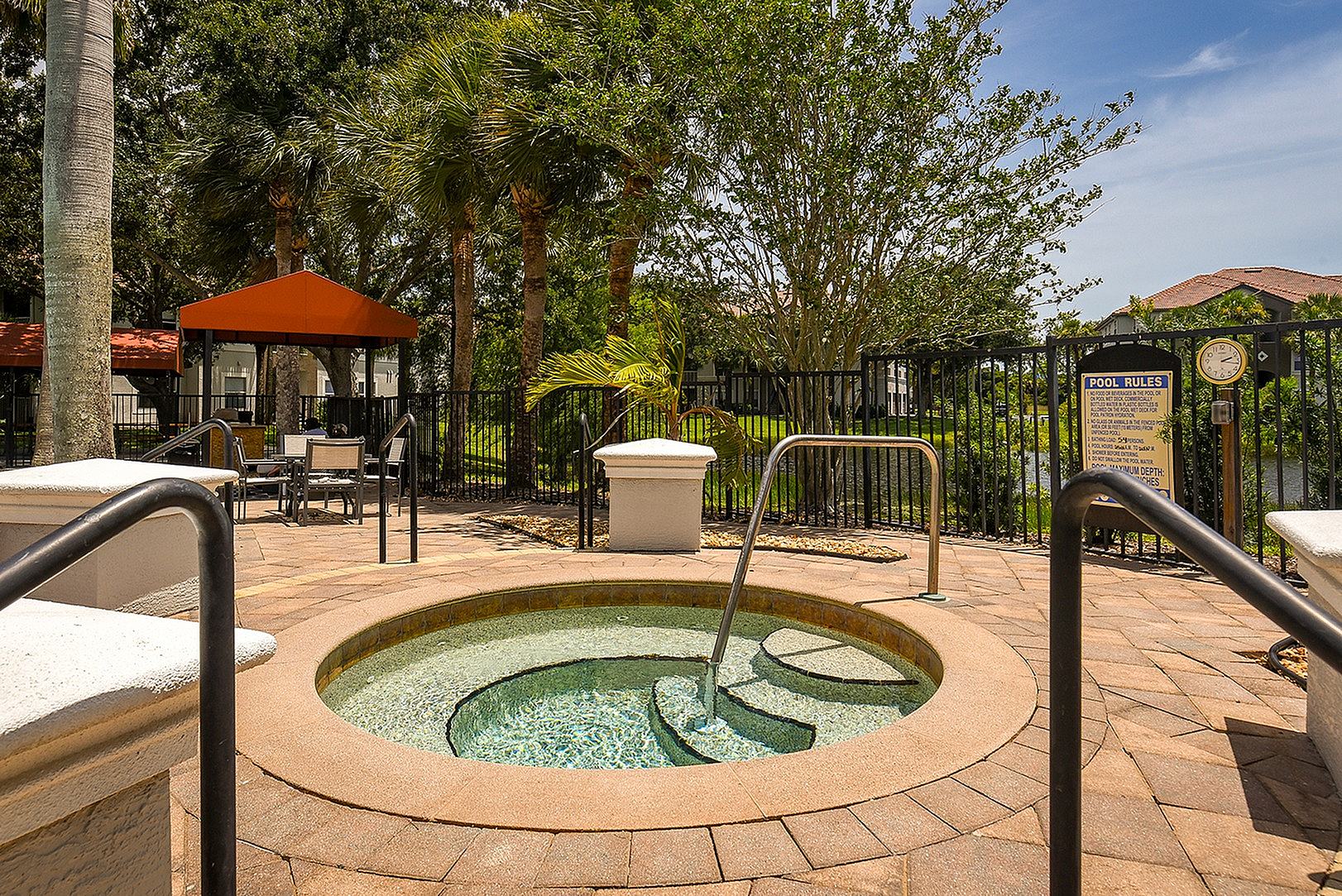Inviting outdoor spa area with a round hot tub surrounded by lush greenery and modern seating under a shaded pergola.