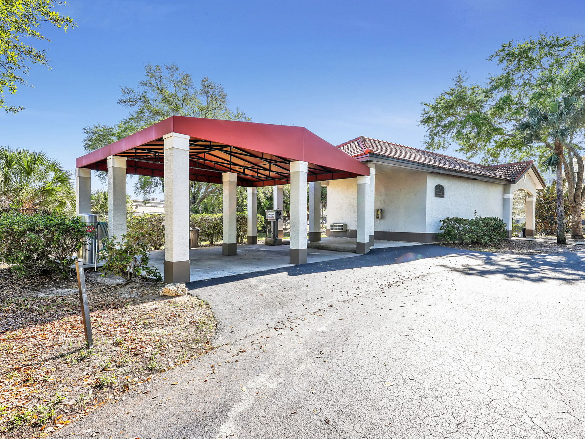 Charming outdoor carport with a red roof near lush greenery, perfect for convenient parking in a tranquil setting.