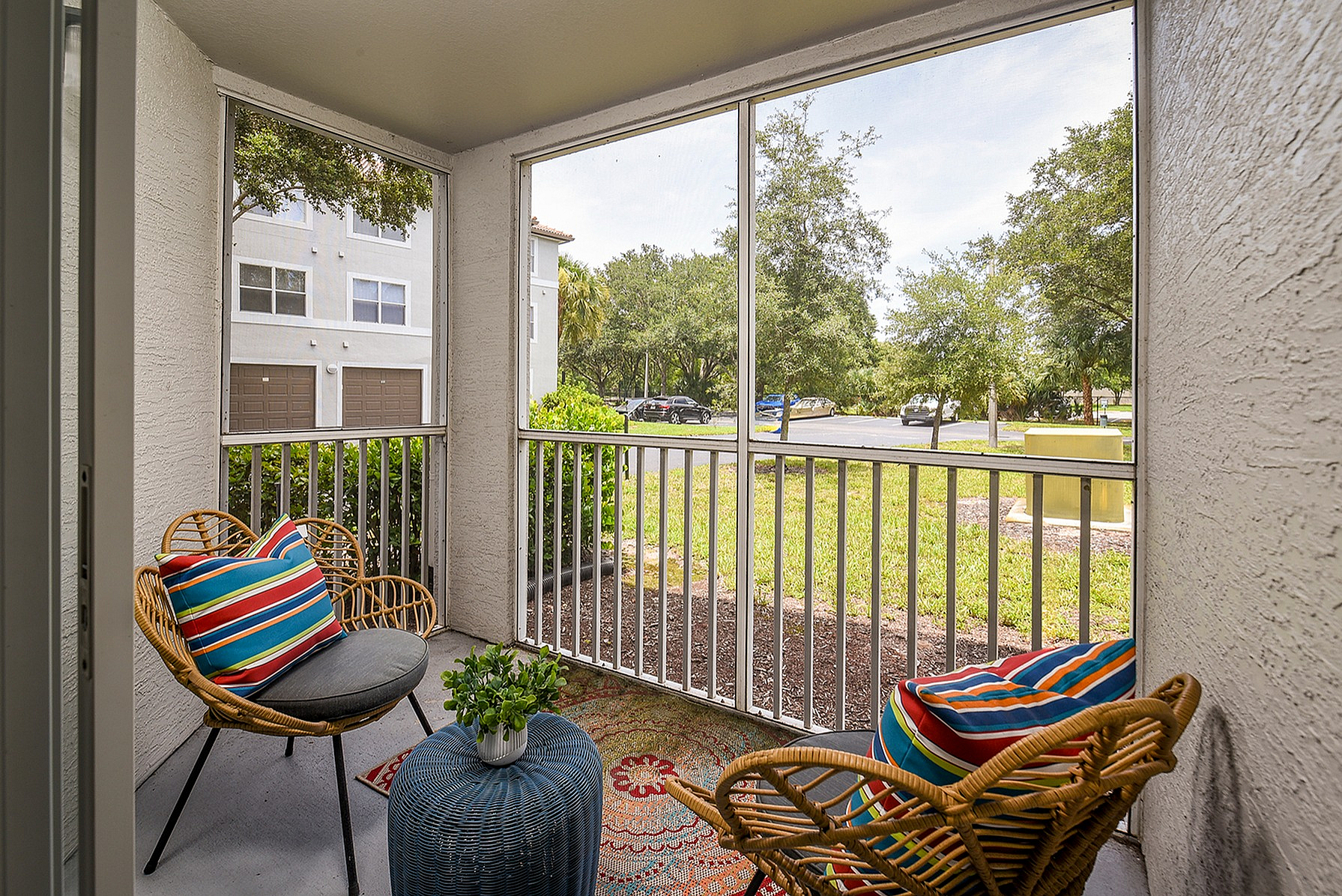 Charming screened patio with colorful seating, overlooking lush greenery and a peaceful community view.