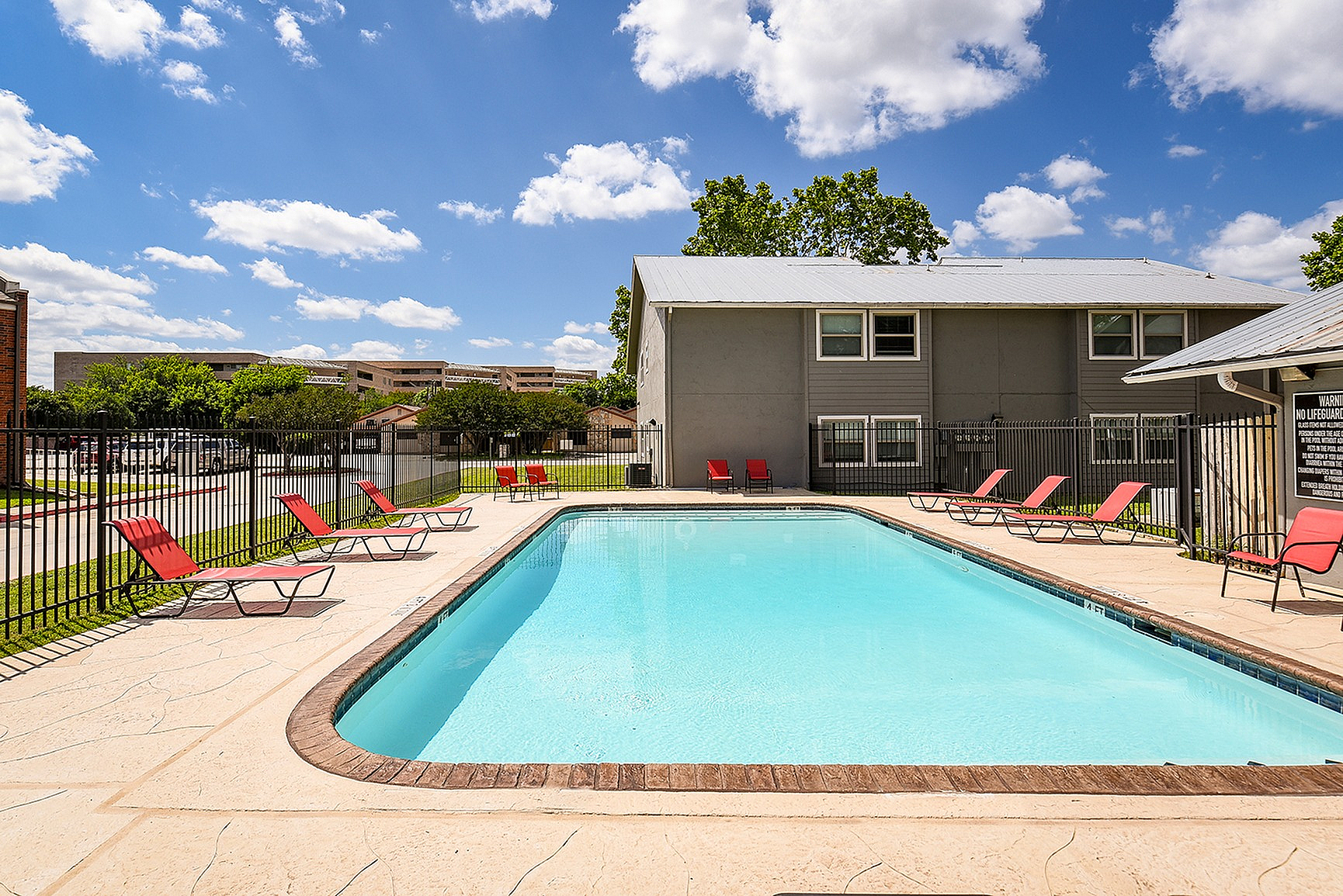 Inviting outdoor pool area with modern red loungers, perfect for relaxation and leisure under the bright blue sky.