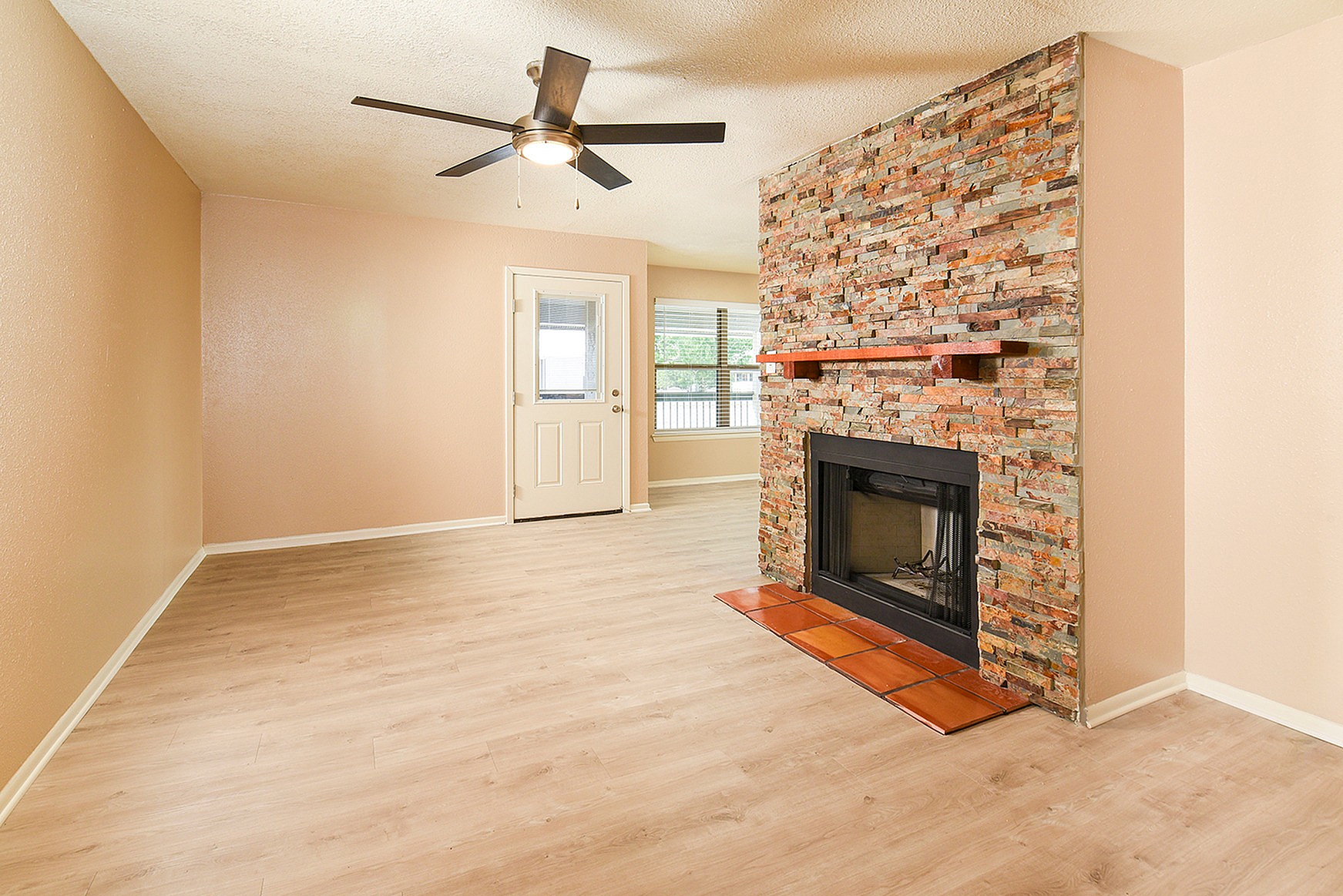 Inviting living room showcasing a rustic brick fireplace, modern ceiling fan, and elegant wood flooring.