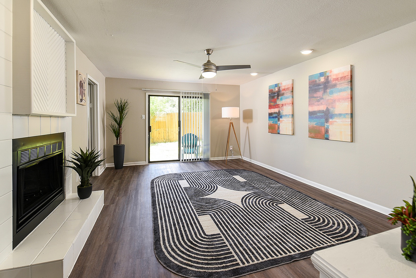 Sunny living room with elegant hardwood floors, vibrant abstract art, modern ceiling fan, stylish fireplace, and sliding glass doors leading to a cozy outdoor space.