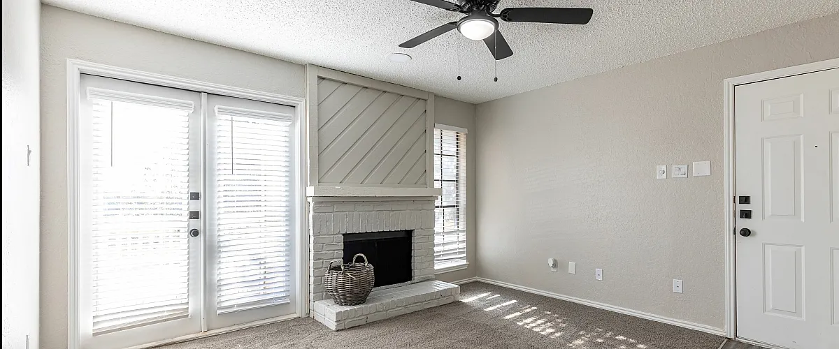 Bright and welcoming living room with plush carpet, modern ceiling fan, and cozy fireplace.