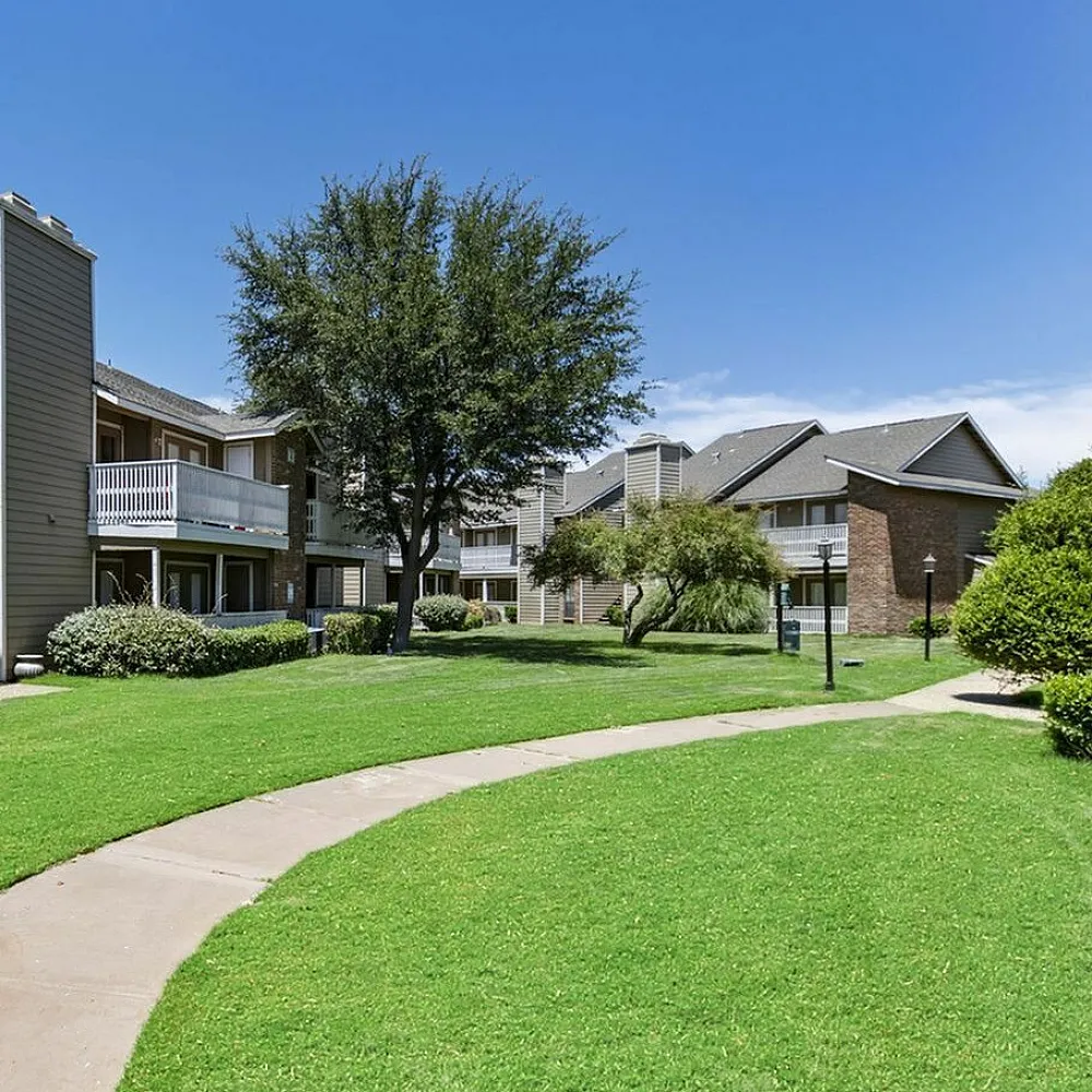 Apartment complex with balconies, lush green lawns, and a winding walkway.