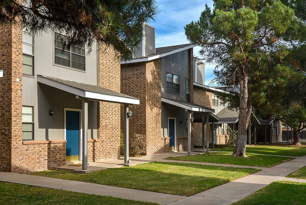 Townhomes with brick facades, blue doors, and lush green lawns.