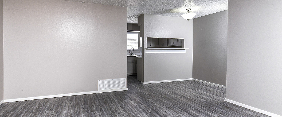 Modern living area with sleek laminate flooring and a view into a bright kitchen.