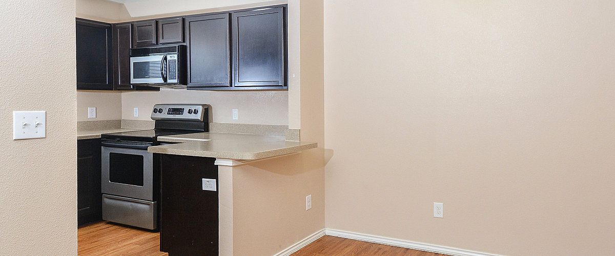 Modern kitchen with dark cabinets, stainless steel appliances, and adjacent dining space with wooden flooring.