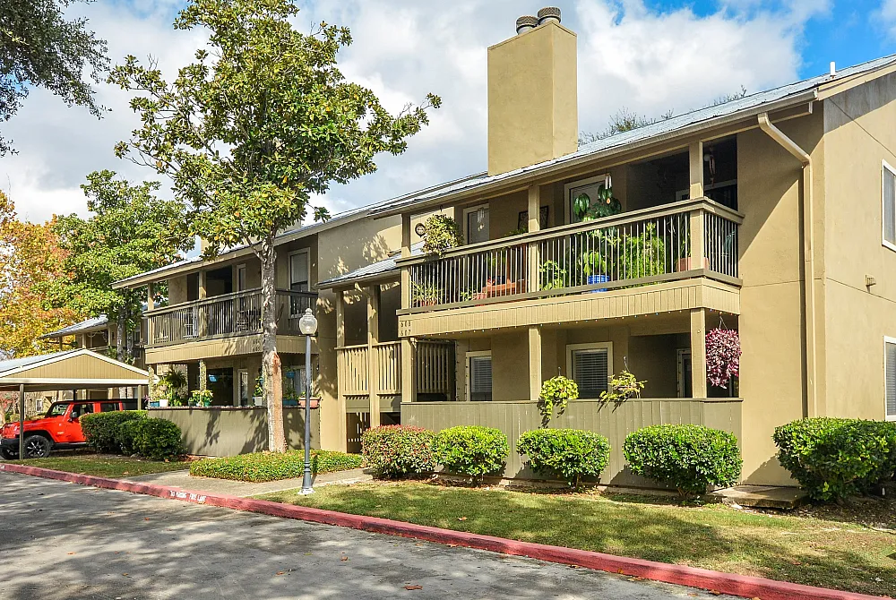 Cozy two-story apartment complex with balconies, lush greenery, and a sunny exterior.