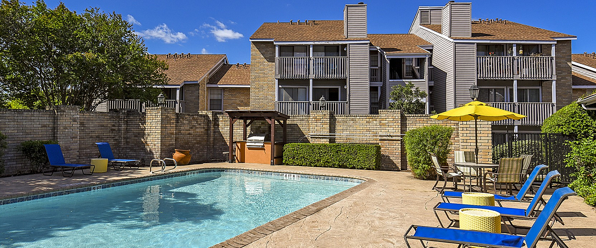 Charming apartment complex with a sunlit swimming pool, inviting lounge chairs, and lush greenery for relaxation and leisure.