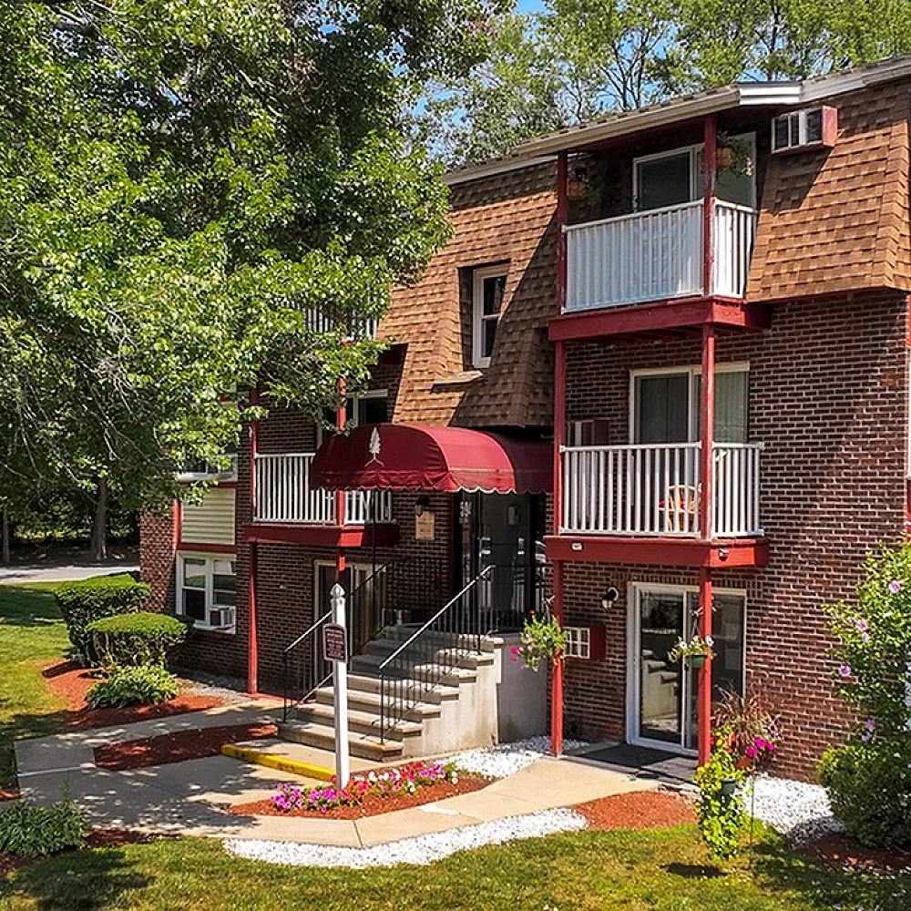 Charming brick apartment building with cozy balconies, surrounded by lush greenery and vibrant gardens.