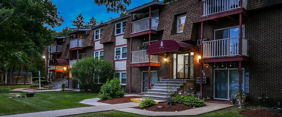 Charming residential building with a classic brick facade surrounded by lush greenery and well-maintained gardens, offering inviting balconies and a serene environment at dusk.