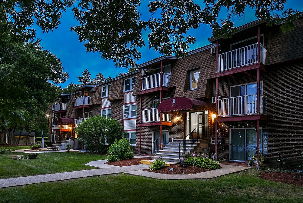 Charming apartment complex surrounded by lush greenery and modern outdoor lighting, creating a welcoming atmosphere.