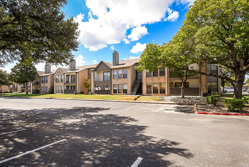 Sunny and inviting apartment complex with lush greenery, ample parking, and charming two-story units.