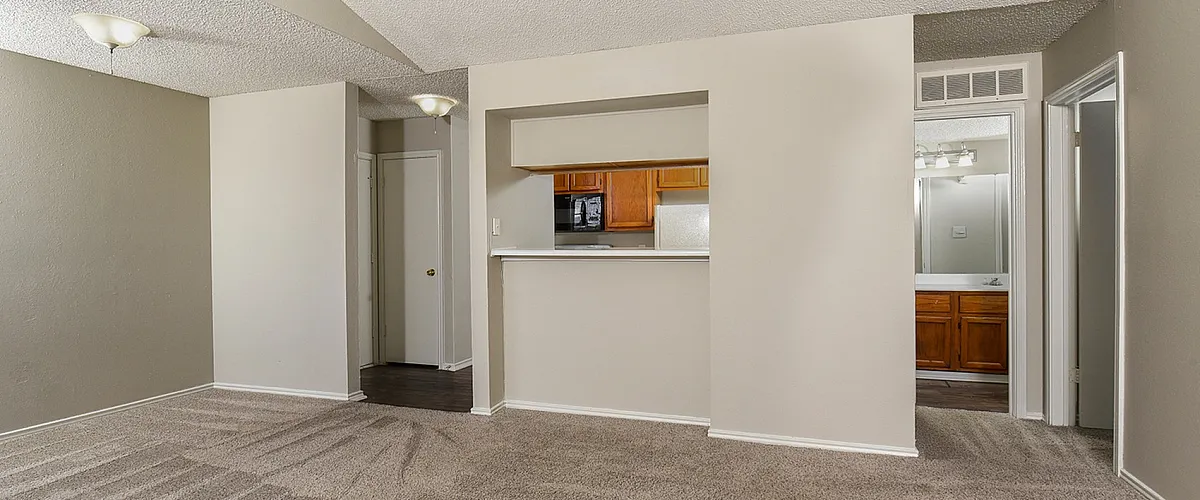 Inviting open-concept living space with plush carpet, modern light fixtures, and a cozy bar counter leading to the kitchen.