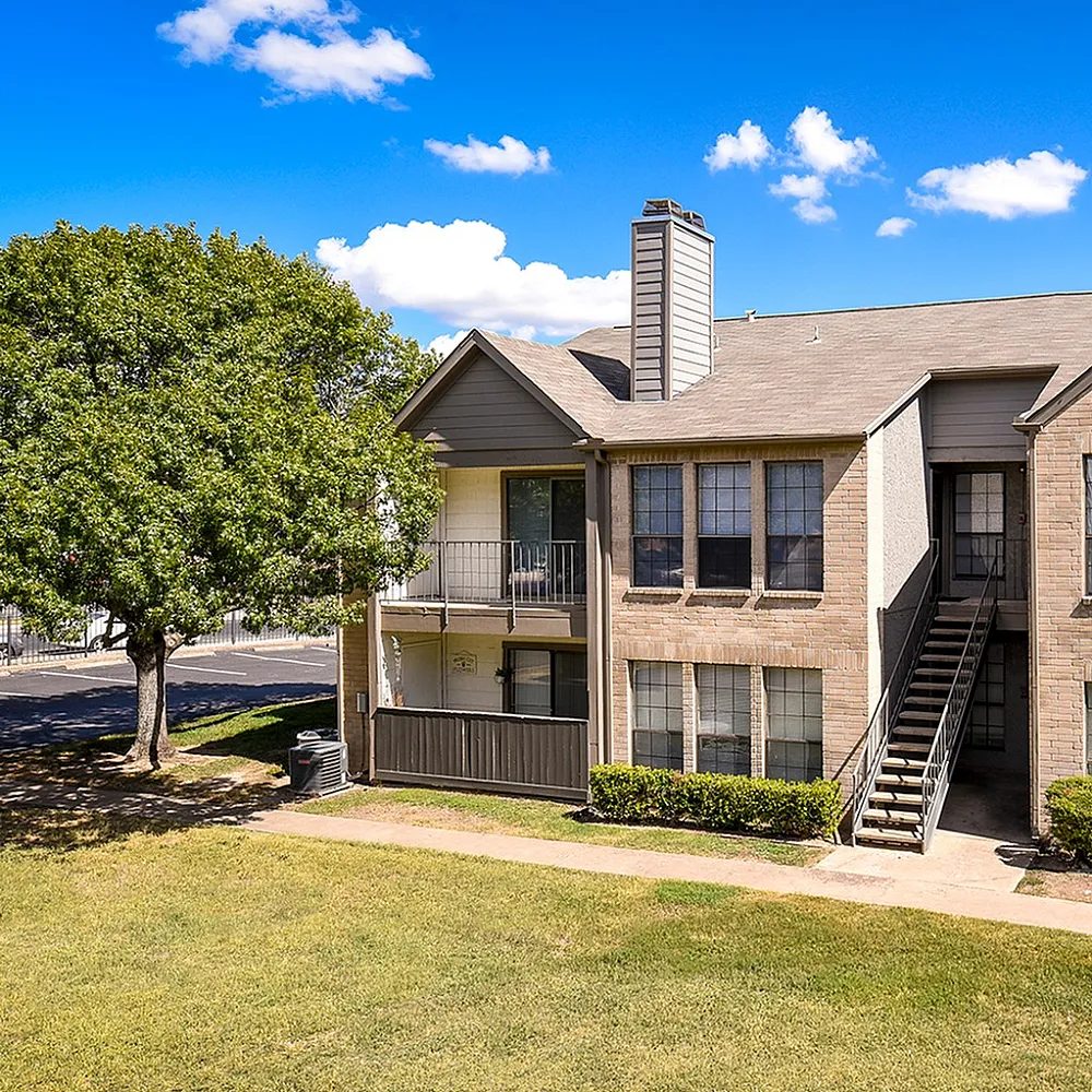 Charming multi-unit apartment building with welcoming balconies, lush greenery, and vibrant blue skies.