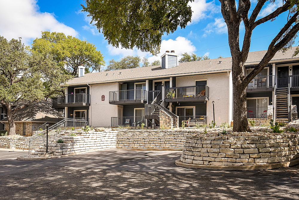 Charming apartment complex with rustic stone accents, spacious balconies, and lush greenery under a blue sky.