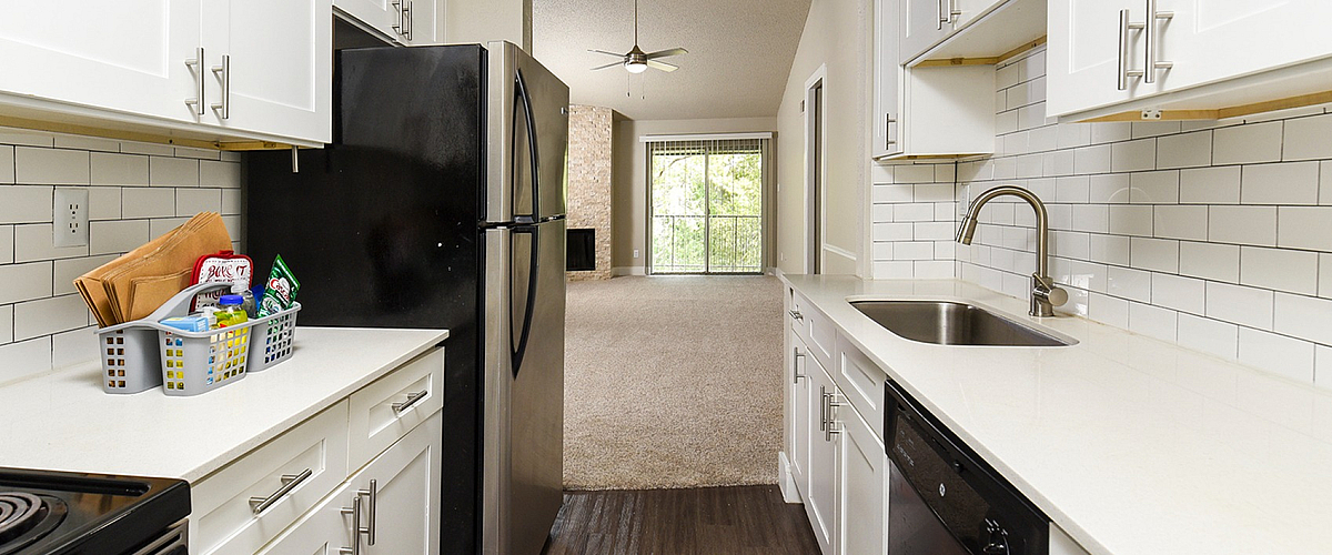 Modern open-concept kitchen with sleek white cabinetry, stylish black appliances, and a cozy view into the inviting living area with natural light.
