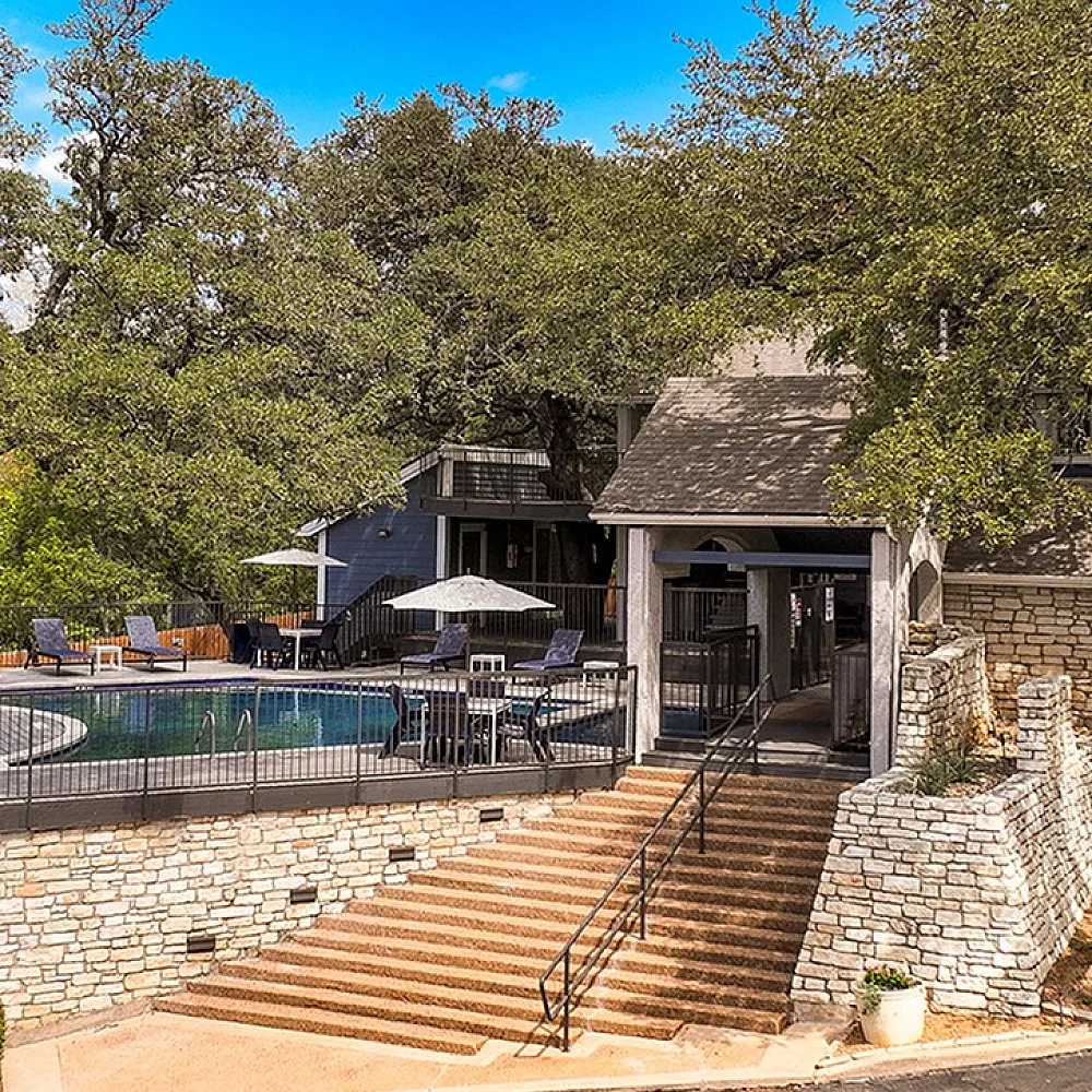 Charming stone-accented apartment complex featuring a serene outdoor pool surrounded by lush trees and inviting lounge chairs.