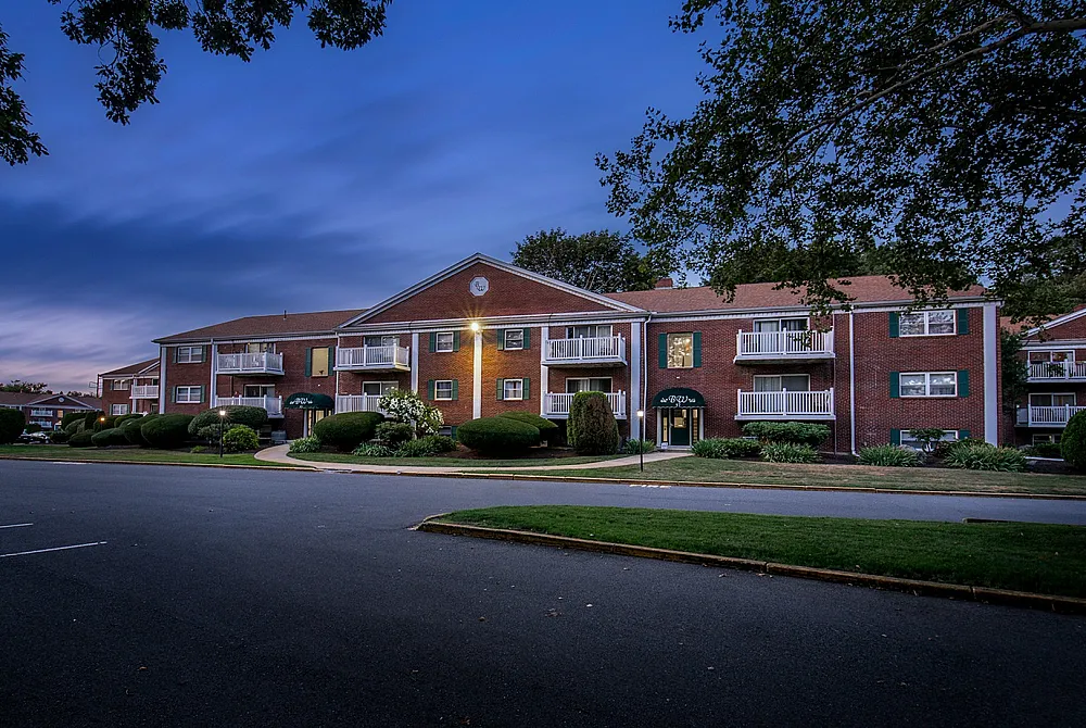 Elegant brick apartment complex at twilight, showcasing charming balconies and well-manicured landscaping.