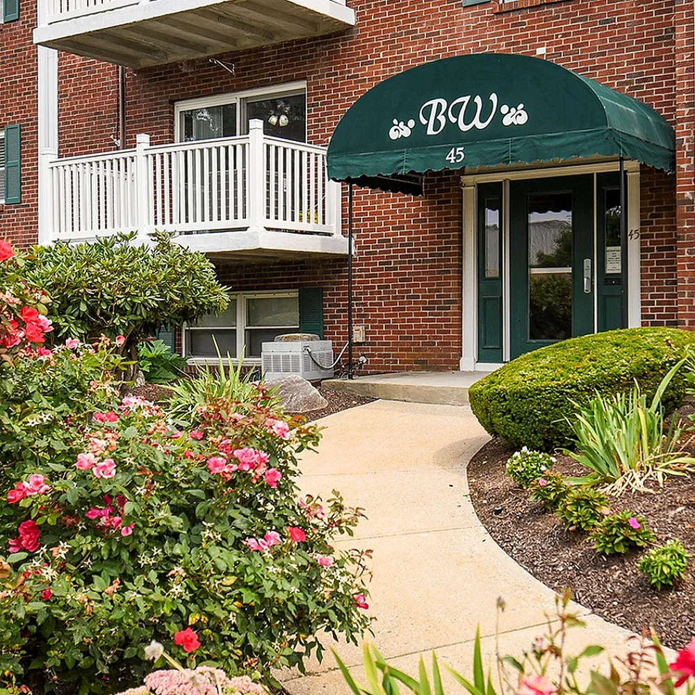 Inviting apartment entrance with lush landscaping and vibrant flowers complementing the building's stylish brick exterior.