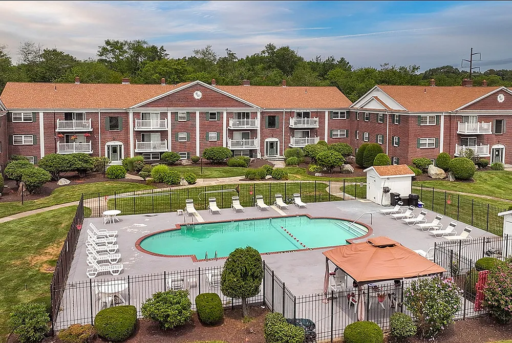 Charming apartment complex with elegant red brick facade, lush greenery, and a refreshing pool, offering serene living in a modern setting.