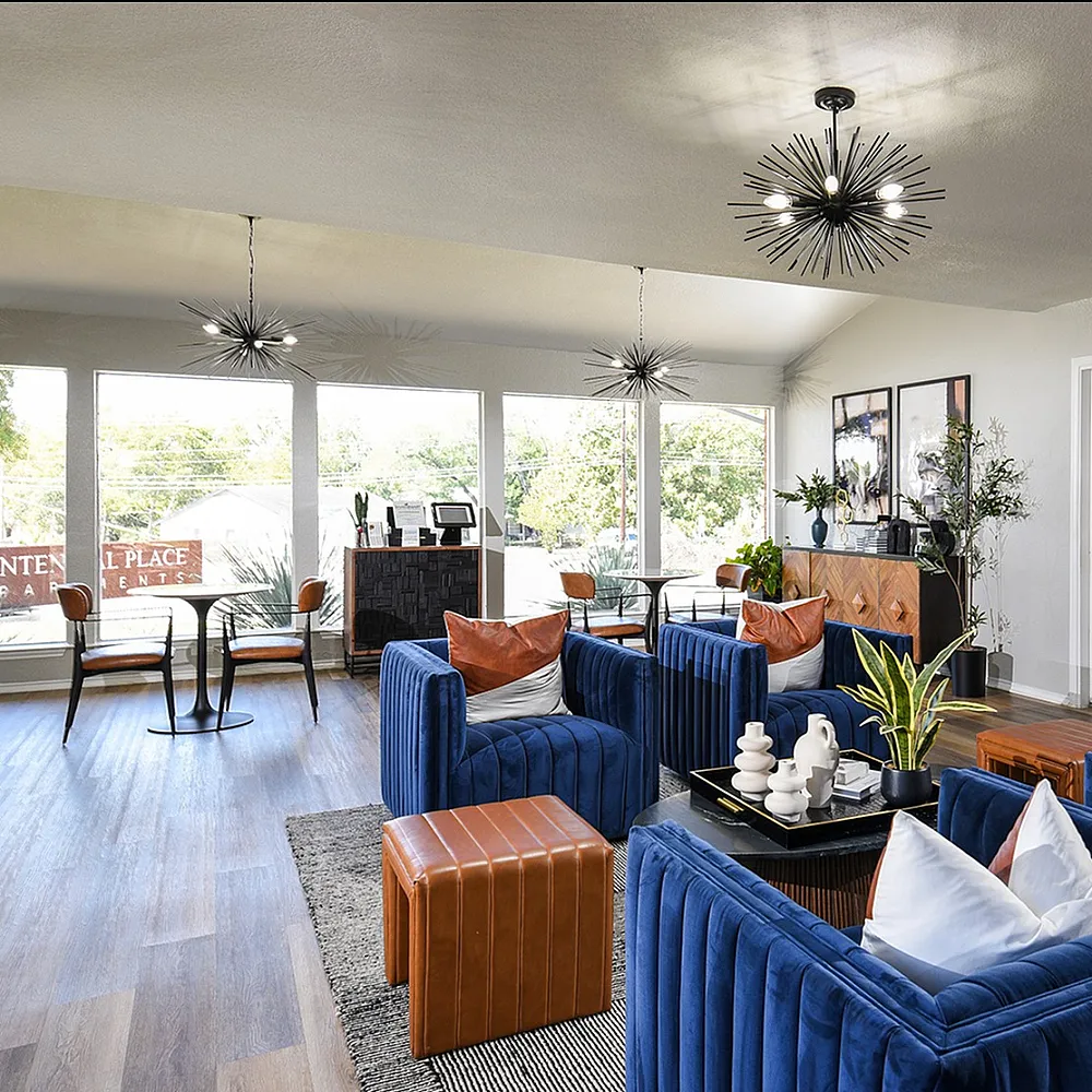 Elegant open-concept living area with plush blue seating, modern lighting, and natural light streaming through large windows.