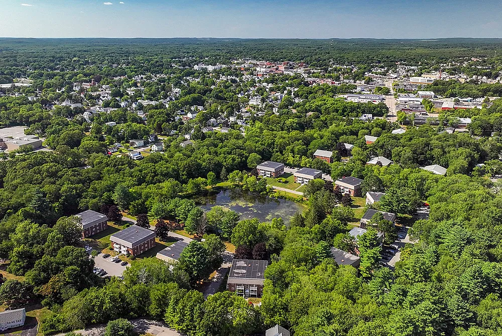 Beautiful aerial view of a tranquil neighborhood surrounded by lush greenery and a serene pond, offering peaceful living in a picturesque setting.