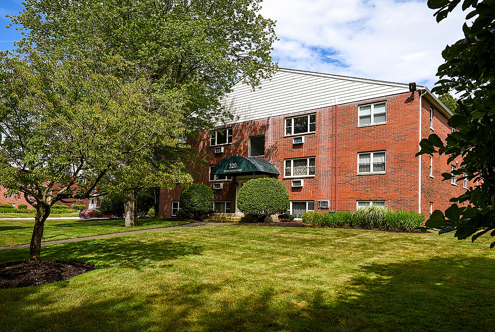 Charming brick apartment building surrounded by lush greenery, offering serene living in a welcoming neighborhood.