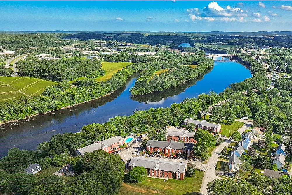 Breathtaking aerial view of a vibrant riverside community with lush greenery, inviting blue waters, and charming residential buildings.