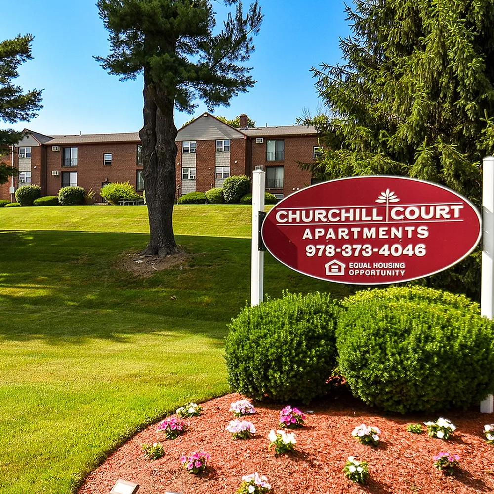Inviting entrance to Churchill Court Apartments, nestled in lush greenery with well-maintained grounds and vibrant flowers.