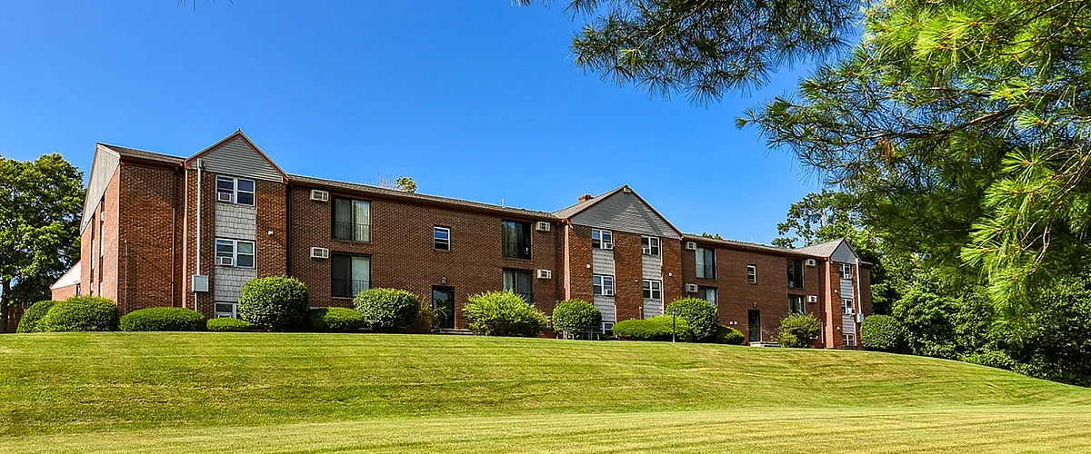 Charming brick apartment complex surrounded by lush greenery under a clear blue sky.