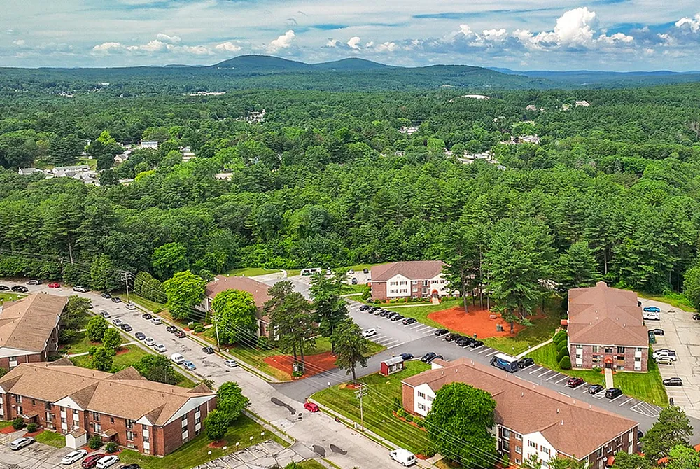 Scenic aerial view of a charming apartment complex surrounded by lush greenery and picturesque mountains, offering an ideal blend of nature and comfortable living.
