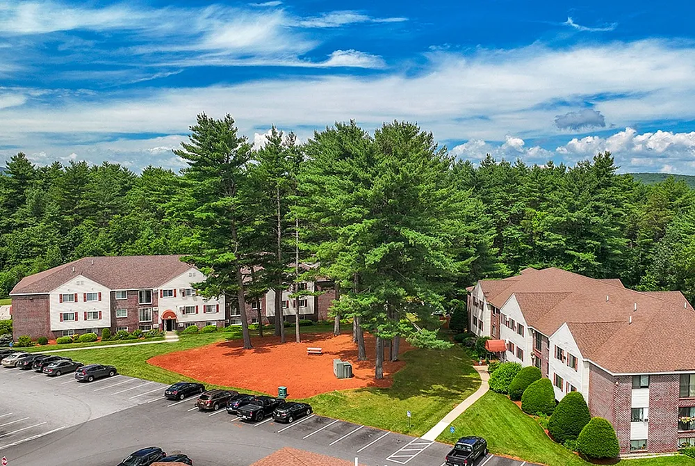 Charming apartment complex nestled amidst lush greenery and rolling hills, featuring ample parking and appealing architectural design.