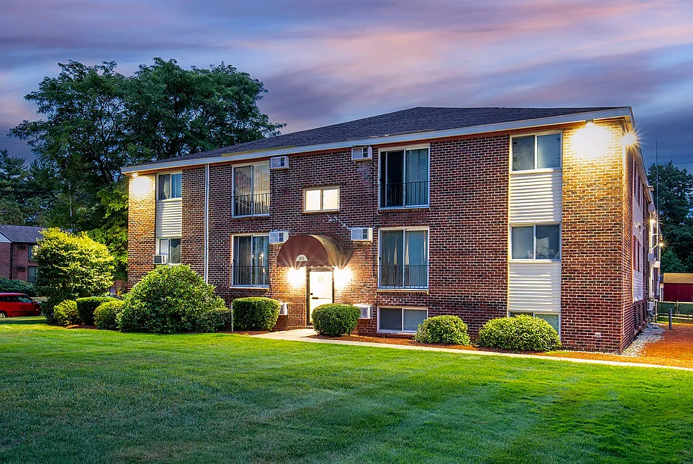 Charming brick apartment building bathed in warm evening light, surrounded by lush greenery and a well-maintained lawn.