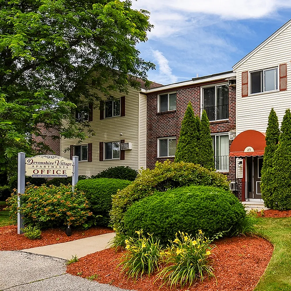 Charming apartment building with manicured landscaping, vibrant greenery, and welcoming office sign under a clear blue sky.