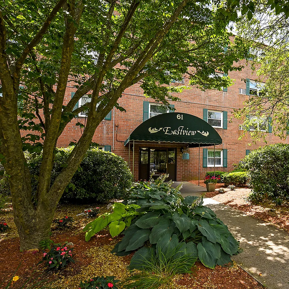 Charming apartment building with lush greenery and welcoming entrance at Eastview, bathed in natural sunlight.