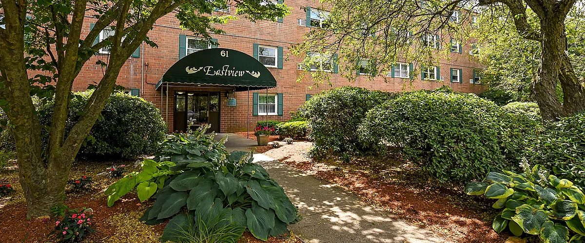 Charming apartment entrance at Eastview with lush greenery and inviting pathway, accentuated by vibrant landscaping and mature trees.