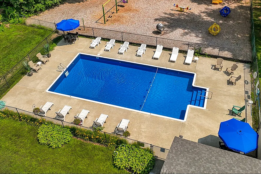 Inviting community pool with sun loungers and vibrant umbrellas, adjacent to a children's play area, surrounded by lush greenery.