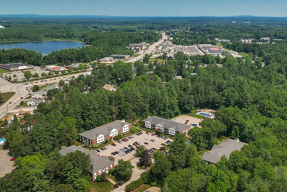 Stunning aerial view of apartment complexes surrounded by lush greenery and nearby a serene lake, showcasing idyllic suburban living.