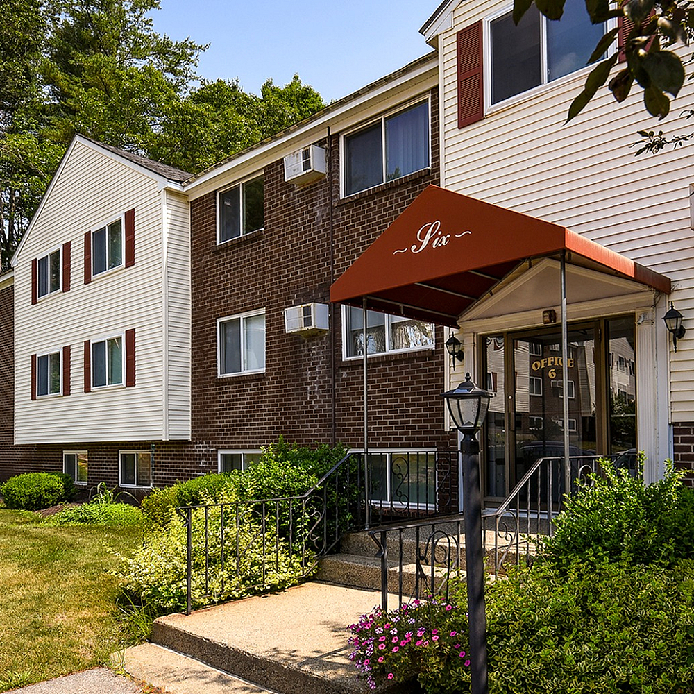 Charming apartment building with a brick and siding exterior, surrounded by lush greenery and inviting entryway.