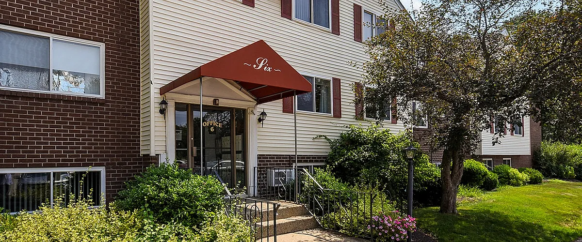 Charming apartment building with brick and siding exterior, surrounded by lush greenery, under a clear blue sky.