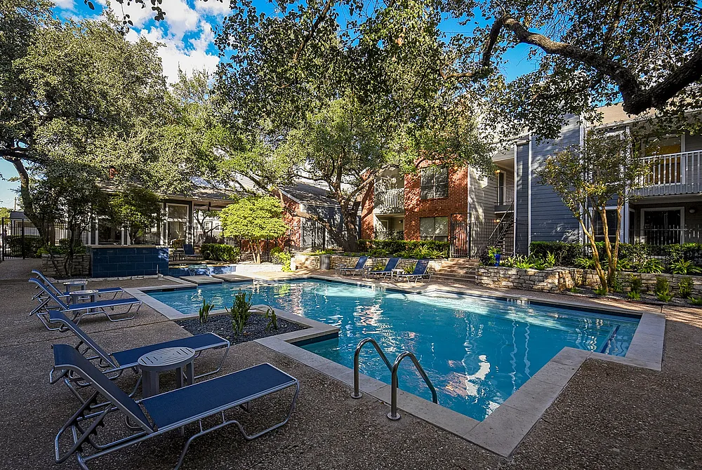 Inviting apartment complex with a sparkling outdoor pool surrounded by lush greenery and comfortable lounge chairs, perfect for relaxation.