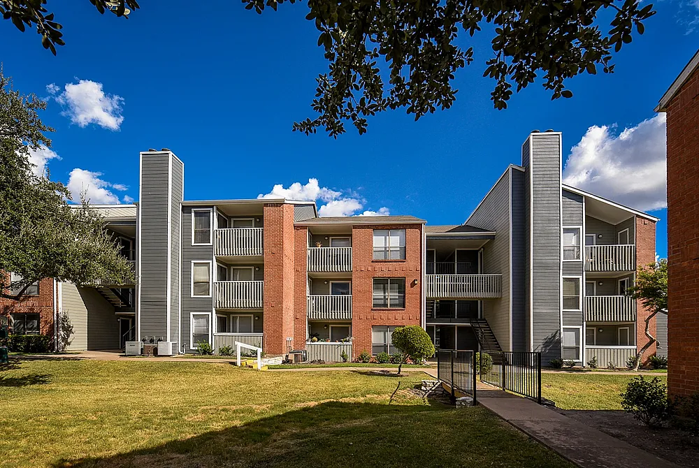 Charming residential building with modern balconies, lush landscaping, and vibrant blue skies.