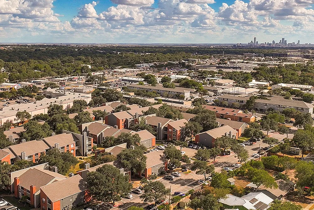 Charming residential neighborhood with modern apartments surrounded by lush greenery, under a picturesque sky and city skyline in the distance.