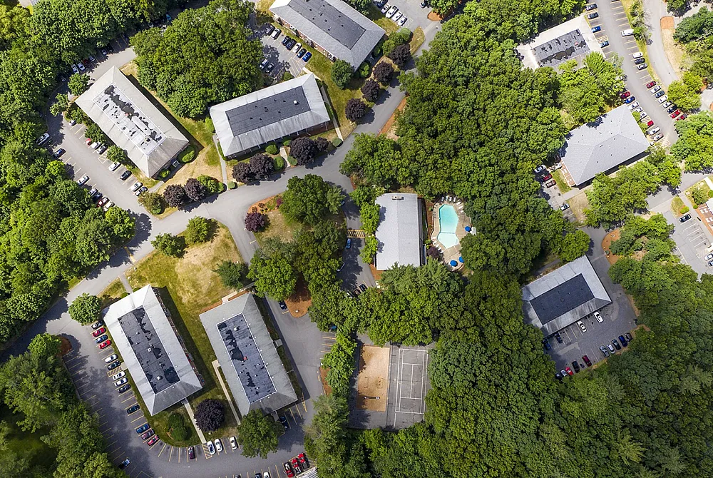 Stunning aerial view of an apartment complex nestled amidst lush greenery, featuring spacious buildings, ample parking, and a refreshing swimming pool.
