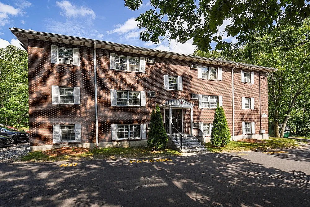 Charming brick apartment building surrounded by lush greenery and ample sunlight, offering a tranquil living environment.