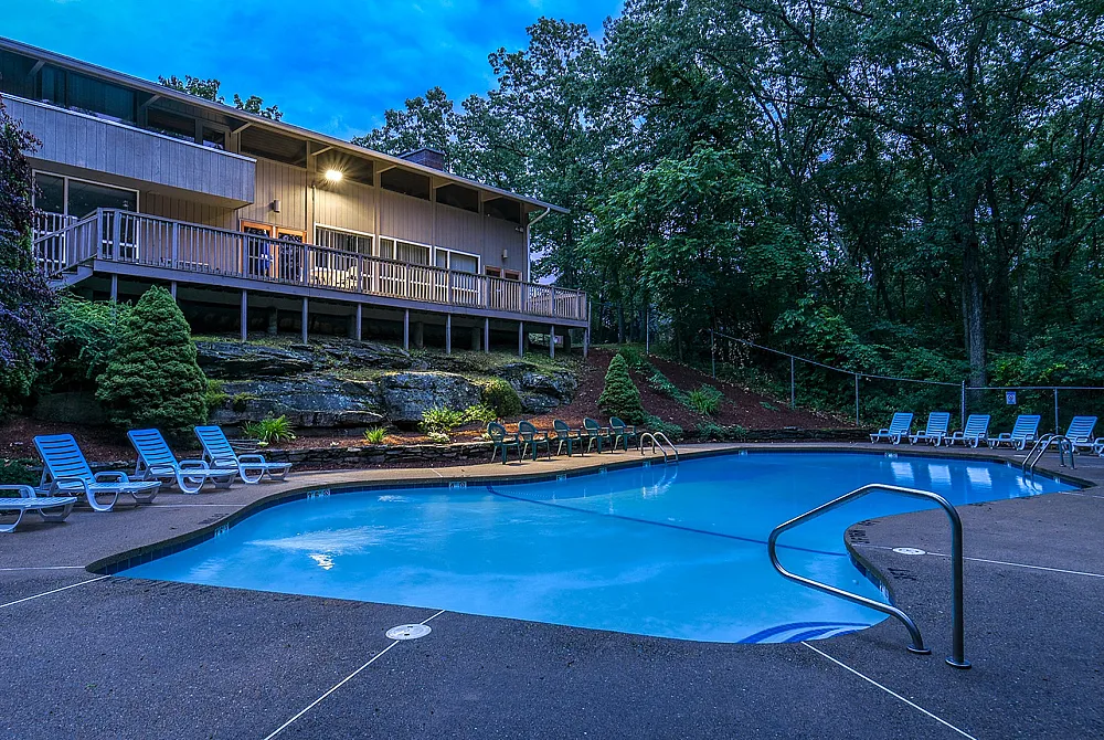 Inviting swimming pool surrounded by lush greenery and modern loungers, adjacent to a charming elevated building with a spacious deck, creating a perfect outdoor retreat.