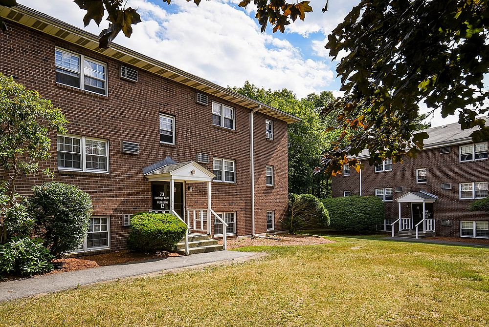 Charming brick apartment building with lush greenery and inviting entryway, perfect for a serene living environment.