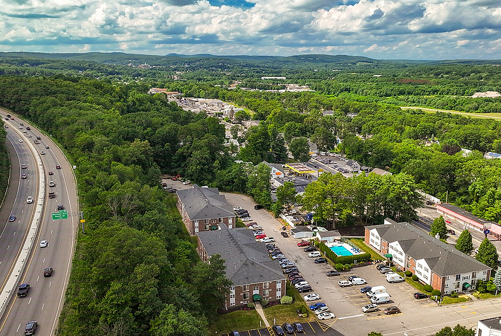Inviting aerial view of a vibrant residential area surrounded by lush greenery, featuring modern apartments and a sparkling blue swimming pool.